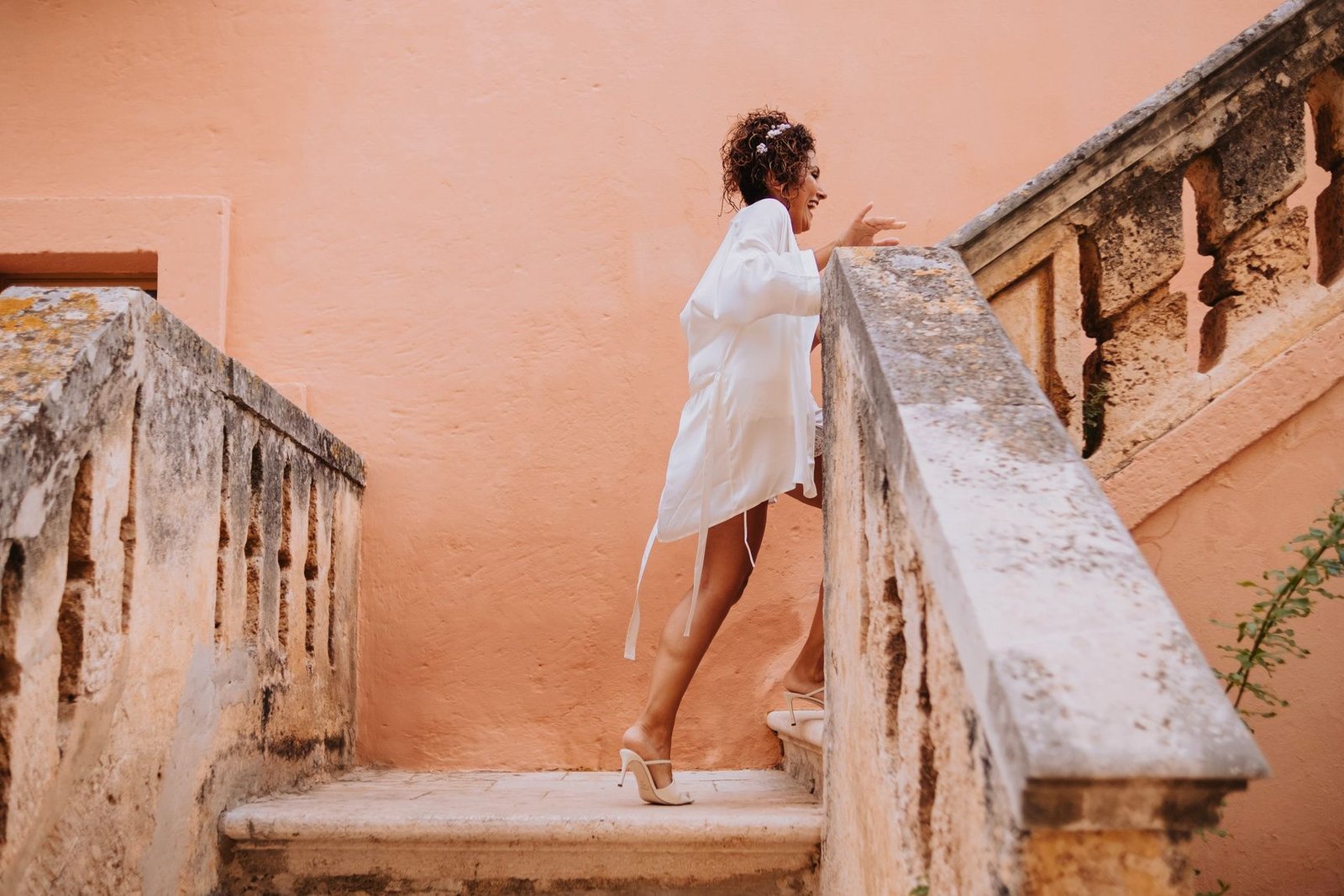Sposa sulla scalinata di una villa pugliese, muro color terracotta